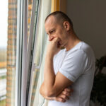 thoughtful entrepreneur leaning against a glass window in his office