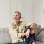 relaxed mature thoughtful man relaxing sitting on sofa and thinking at home.