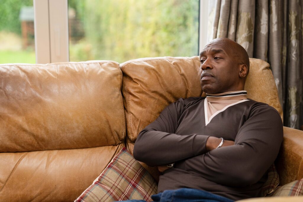 man sits on a couch with arms crossed while deep in thought in a cozy living room setting