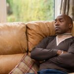 man sits on a couch with arms crossed while deep in thought in a cozy living room setting