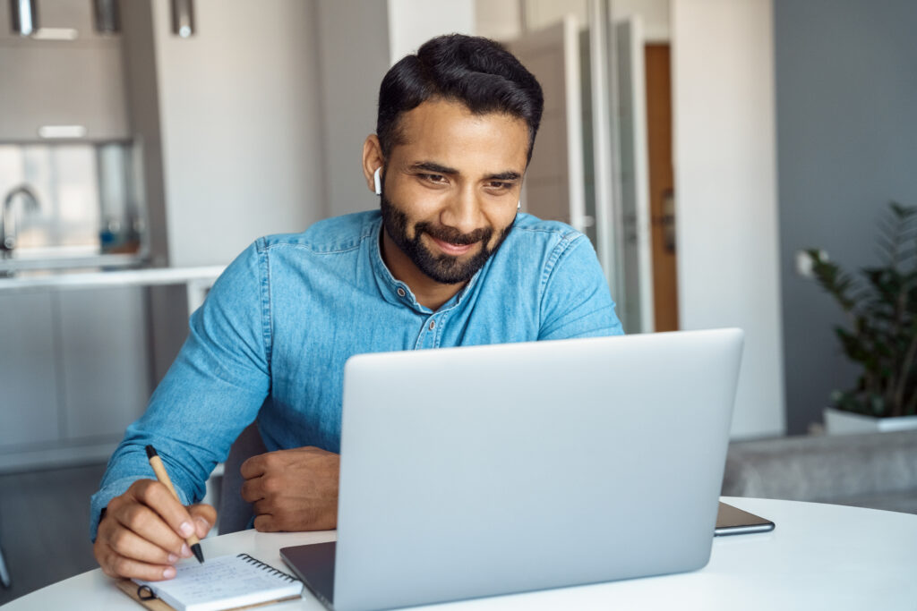 portrait of young adult indian man wearing earphones looking at laptop screen