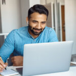 portrait of young adult indian man wearing earphones looking at laptop screen